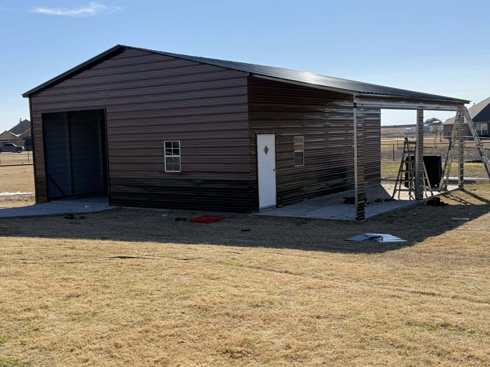Brown metal workshop garage with roll-up door and attached lean-to carport
